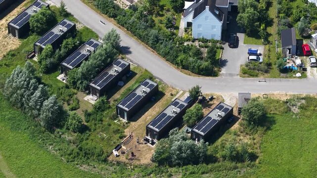 Aerial view of tiny houses in an eco village, showcasing self sufficient living, solar panels, green residential design and a sustainable community setting.