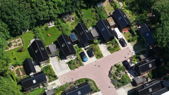 Aerial view of tiny houses in an eco village, showcasing self sufficient living, solar panels, green residential design and a sustainable community setting.
