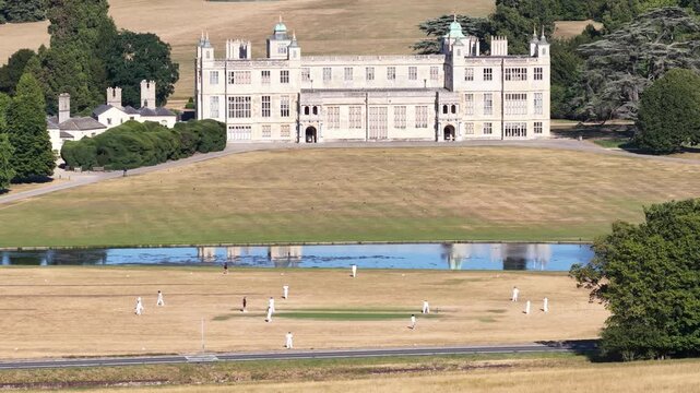 Traditional cricket match unfolding on a sun scorched pitch with the magnificent jacobean mansion audley end house providing a historic and quintessentially english country background
