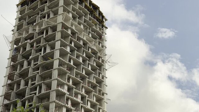 A massive concrete highrise frame stands tall during construction under shifting clouds. The incomplete structure looks powerful yet desolate, inspiring a sense of quiet anticipation.