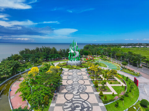 Kecamatan Bulak, Jawa Timur, Indonesia - 02 May 2026: Aerial view of Suroboyo Park with its iconic shark and crocodile statue, lush gardens, patterned walkways, and the coastline.