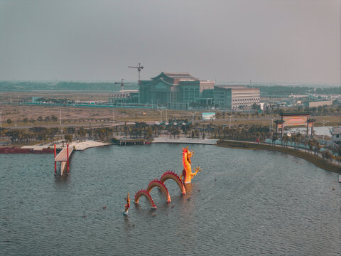 Teluknaga, Banten, Indonesia - 26 June 2026: Aerial view of Patung Naga Air Pik in the lake, with a large building complex and construction cranes in the background.