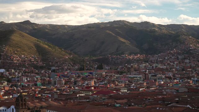 Cusco Panoramic Plaza de Armas main square city of Cuzco Peru cityscape landscape rainy season sunset golden hour clouds Peruvian neighborhood buildings on mountainside Anta Province Andes pan left