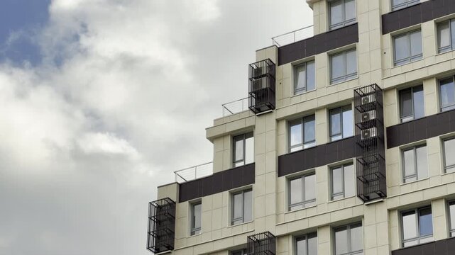 A modern apartment building features a clean, geometric facade with unique metal air conditioner cages. The orderly design feels calm, professional, and slightly sterile against the soft, cloudy sky.
