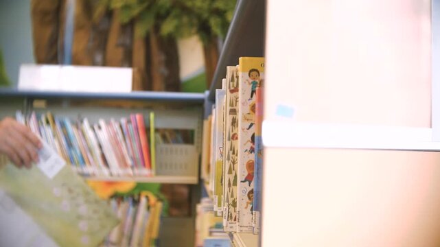 A hand reaches out to pull out a children's book from a book shelf at a library on a warm summer day.