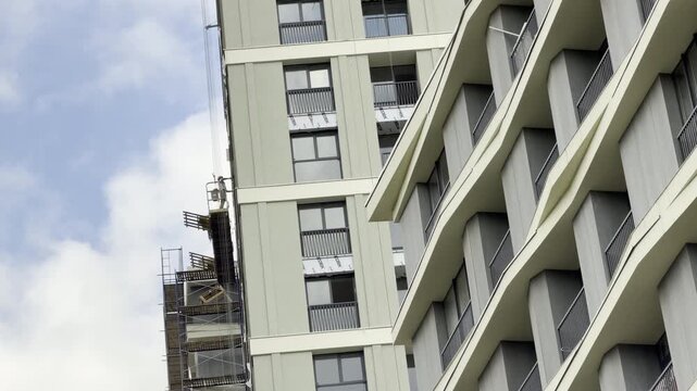 Modern apartment skyscrapers rise against a cloudy sky during construction. The active site evokes feelings of progress and ambitious urban development in this tall architectural setting.