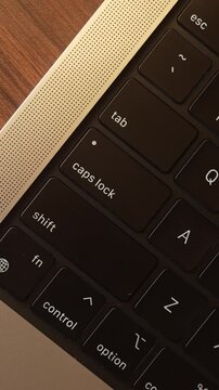 Finger Pressing Caps Lock Button on Laptop Keyboard in Warm Lighted Room.
