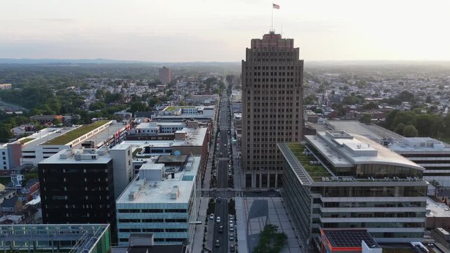 PPL Building art deco tower rises above downtown Allentown Pennsylvania at golden sunset, cars travel wide boulevard past modern glass office buildings and green rooftops. Aerial drone wide shot