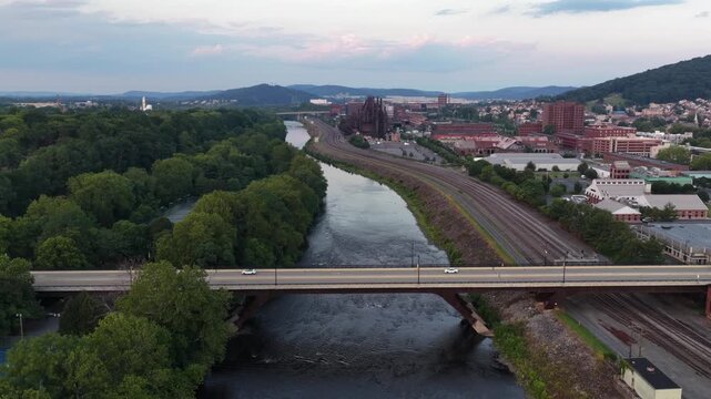 Highway bridge carries cars over Lehigh River near Bethlehem Steel Stacks in Bethlehem, Pennsylvania, railroad tracks and wooded hillsides spread beside quiet downtown. Aerial drone wide shot