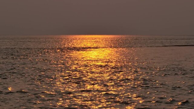 Sunset seascape background. Ocean water reflecting vibrant orange and yellow hues of low sun during a serene evening golden hour at sea in Thailand, creating a peaceful and shimmering surface horizon