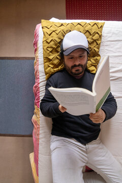 Top down view of a man lying on a bed reading a book