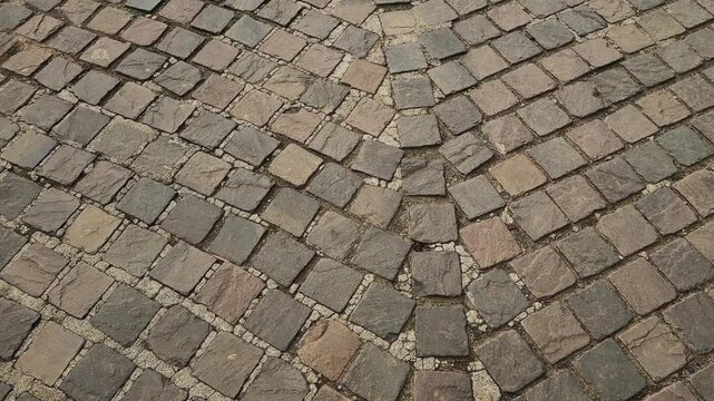 Forward tracking shot over an intricately laid cobblestone pavement showcasing textured natural stone blocks arranged in elegant curved patterns