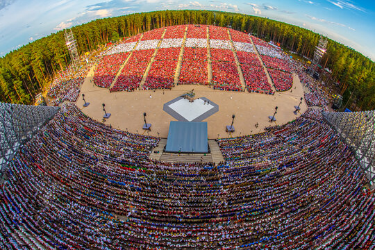Riga, Latvia - 13 July 2025: Aerial view of Mezaparks open-air stage filled with a massive crowd of people during a large cultural event, surrounded by dense pine forest.