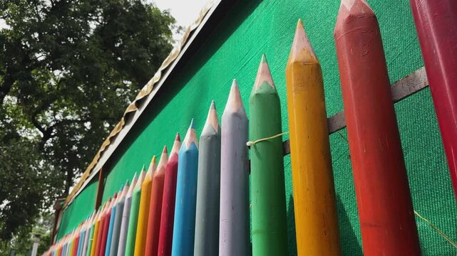 Push in shot of oversized colorful pencil fence decoration installed along a school boundary wall representing creativity education and child friendly public space