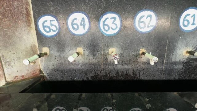Left to right tracking shot of numbered drinking water taps with a dripping faucet in a public facility in indian railway station