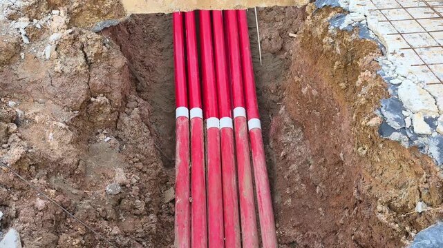Multiple HDPE pipes are installed inside a ground trench at a construction site. These pipelines will be buried after inspection. They serve as conduits for high voltage electrical cables.