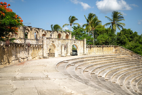 La Romana, La Romana, Dominican Republic - 22 July 2026: Aerial view of Altos de Chavon Amphitheatre, featuring stone tiered seating, arched walls, and palm trees under a blue sky.