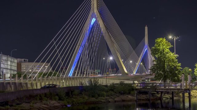 The Zakim Bridge in Boston is illuminated at night, with traffic flowing on the highway below.