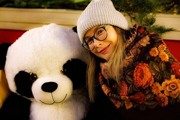 Enjoying a cozy moment with a giant panda stuffed toy during a winter festival © AlexKriv