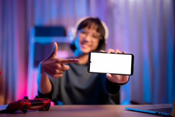 Young person showcasing a blank smartphone screen while sitting at a desk with a gaming controller © 2B