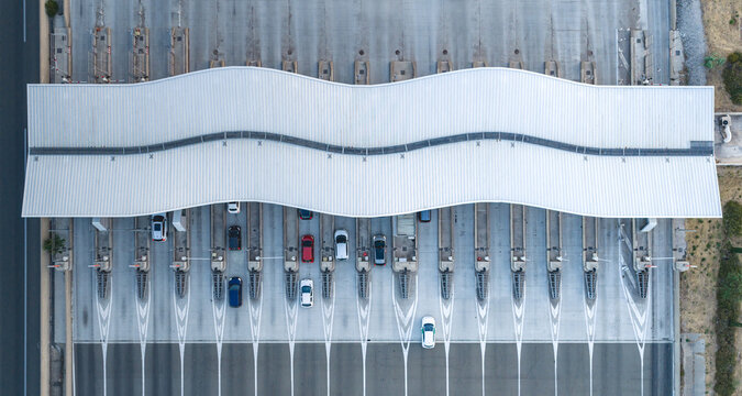 Baillargues, France - 18 July 2026: Aerial view of a modern highway toll plaza featuring a distinctive wave-shaped roof, precise lane markings, and several cars passing through the booths.