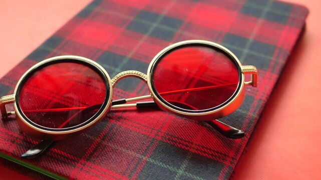 Stylish round red sunglasses resting on a red and black checkered fabric