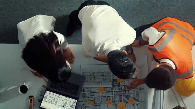 Top view of smart architect and skilled civil engineer team working together to design building construction while standing at meeting table with blueprint, equipment and safety helmet. Alimentation.