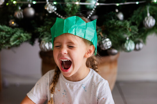 Australian child sitting under Christmas tree wearing green paper cracker hat and laughing