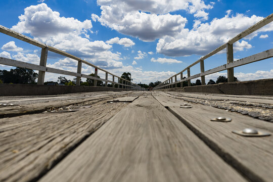 Long angled view along an abandoned wooden bridge with puffy clouds in a blue sky above