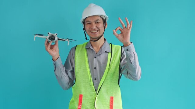 Construction engineer holding drone and gesturing OK sign with smile on cyan studio background