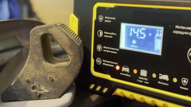 A smart battery charger runs inside a workshop garage. The electronic device charges a vehicle battery. This operation produces a continuous low humming sound.