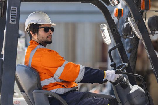 Forklift operator driving industrial forklift in warehouse, wearing safety helmet, gloves and high visibility uniform. Material handling, warehouse logistics, workplace safety, supply chain.