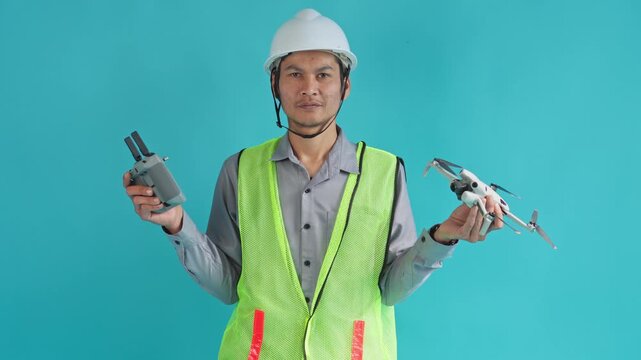 Construction engineer holding drone and remote controller while looking between both on cyan background