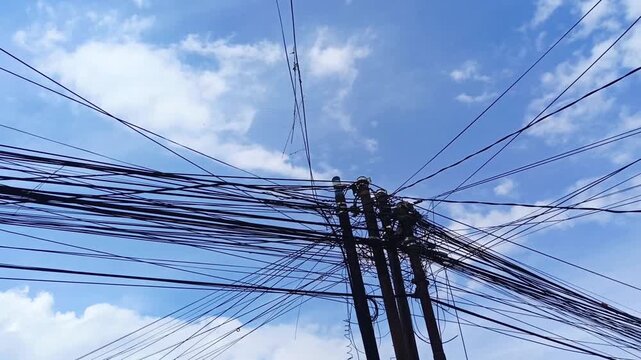 Tangled electrical cables on utility pole against blue sky