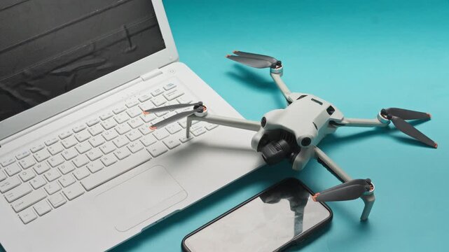 Hand placing modern mini drone next to laptop and smartphone against cyan background