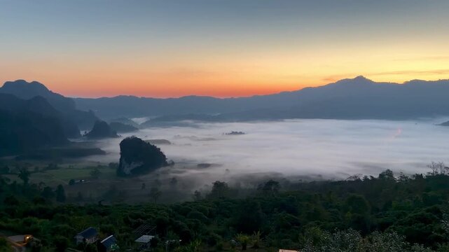 Cinematic panoramic sunrise revealing a dense blanket of morning fog rolling through the mountain valley in Pong, Phayao, Thailand.