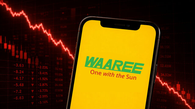 Waaree Energies logo displayed on a yellow-screen smartphone held before a declining red stock chart, illustrating bearish market sentiment.