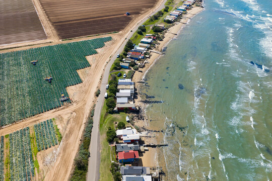 Aerial view of a row of coastal fishing cottages between market garden crops and the sea