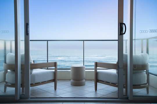Two outdoor chairs and a small table are positioned on a tiled balcony overlooking the ocean.