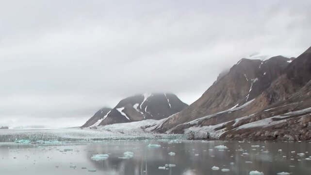 A breathtaking view of a massive glacier flowing into the icy Arctic sea. Ice floes drift gently on the calm water, reflecting majestic snow-capped mountains under an overcast sky.