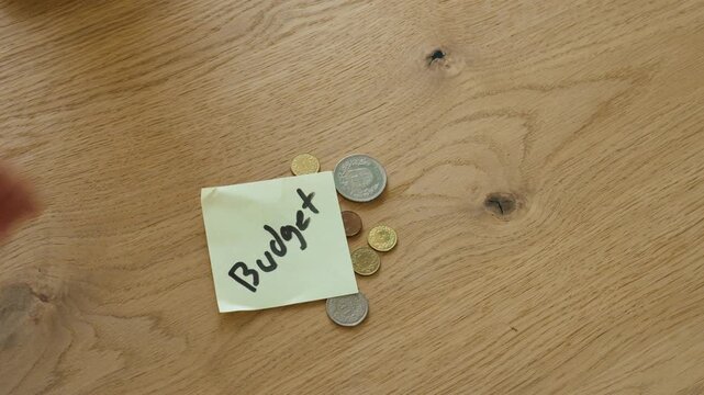 A hand counts coins before placing a sticky note labeled "Budget" on top of them. Concept of budgeting, saving money, personal finance, and expense management.