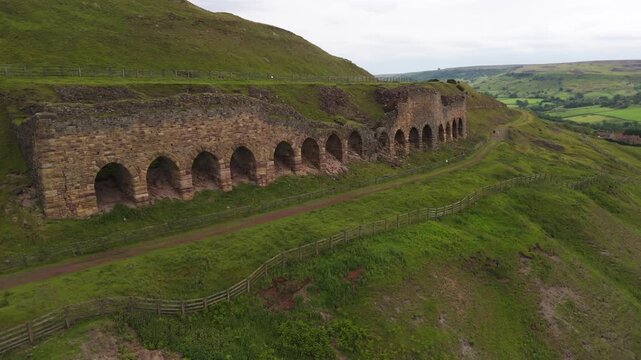 drone view around the abandoned historic stone ironstone kilns in Rosedale Abbey, set against overcast rolling Yorkshire hills.