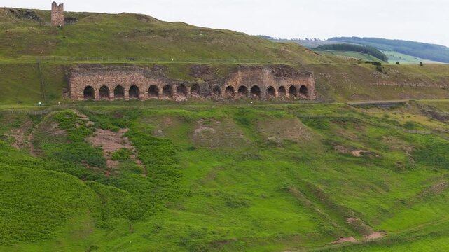 drone flying around the abandoned historic stone ironstone kilns in Rosedale Abbey, set against overcast rolling Yorkshire hills.