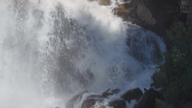 A heavy volume of water surges down the rocky cliff side of Inglis Falls during spring. The rushing white water pounds against dark limestone boulders in Owen Sound, Ontario.