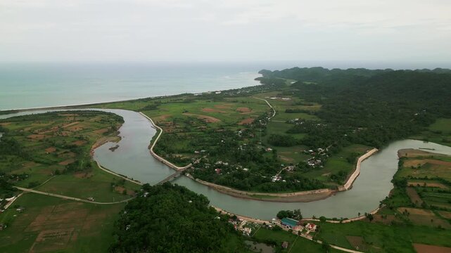 Aerial drone shot of wide, curved Pajo River with surrounding farmlands, coastal greenery, and rural terrain - Catanduanes, Bicol, Philippines