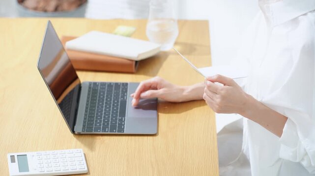 通帳とノートPCを見る女性。貯金、銀行、投資、財テク、節約、マネー、お金、貯蓄、DX、家計、金融