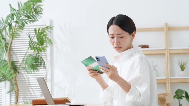 通帳とスマホを見ながら悩むミドル女性。貯金、節約、ローン、アプリ、家計、銀行、給料、不満、心配、不安