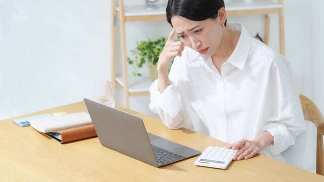 ノートパソコンを見ながら悩むミドル女性。家計、経理、事務、不安、心配、不満、疑問、経営、電卓、DX