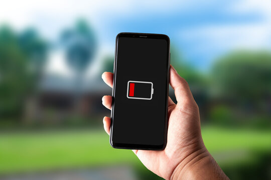 Hand holding smartphone displaying low battery red icon on screen