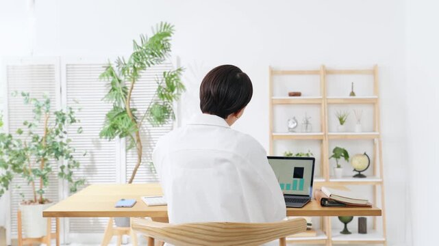 A woman seen from behind, looking troubled while gazing at her laptop. Work, household finances, anxiety, worry, dissatisfaction, questions, deep thought, trouble.